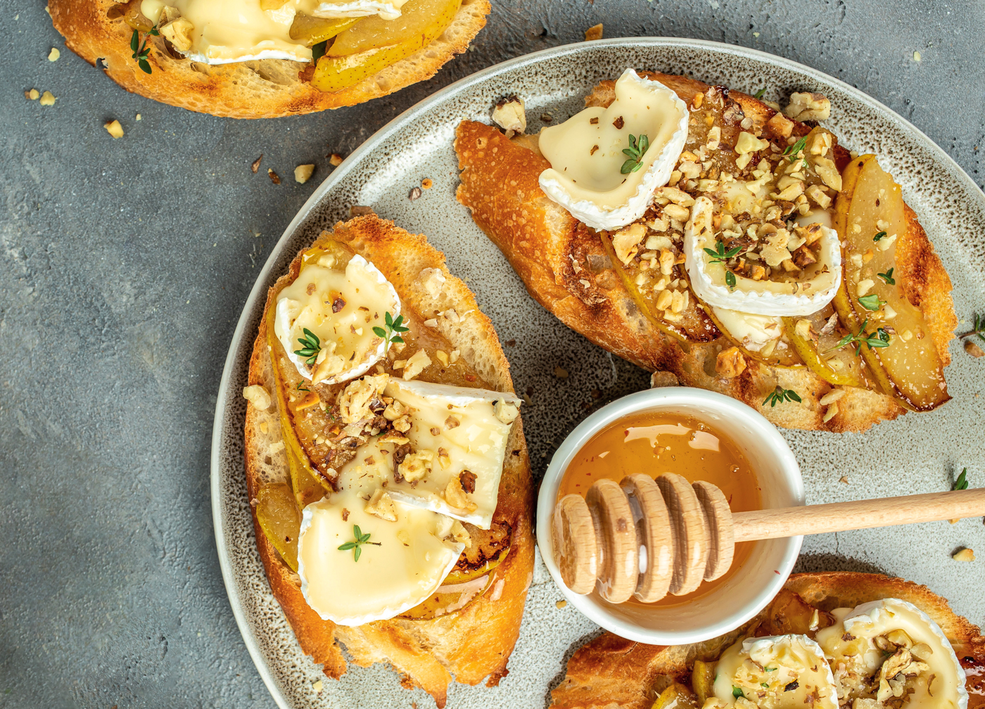 Overhead photo of crusty bread with brie, pears, honey, and nuts.