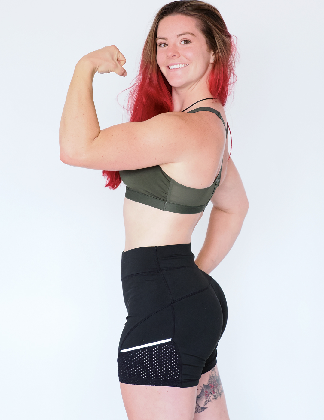 Hélina Bear in black shorts and a khaki green sports bra in front of a white background.
